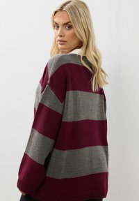 Stickad tröja med djärva vinröda och grå ränder, avslappnad passform, ribbade manschetter och nederkant, med en mjuk textur och rundad halsringning.