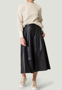 Crème-kleurige trui met geribbelde manchetten, gecombineerd met een zwarte leren midi-rok met een vloeiende uitstraling, en beige sneakers.