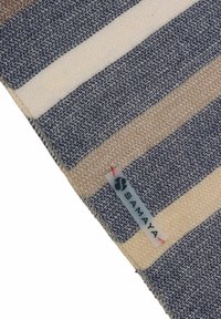 Woven blanket in blue, beige, and cream stripes. Features a textured fabric with a visible brand label in the bottom corner.