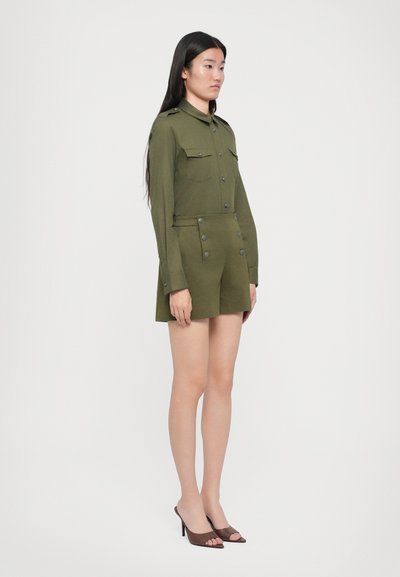Olivnozeleni vojaški slog obleka z dolgimi rokavi, dvema žepoma na prsih in prilegajočim pasom. Sprednji del odlikujejo dekorativni gumbi in kratek rob.