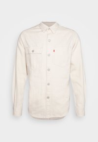 Camicia a maniche lunghe di colore crema realizzata in cotone. Presenta un colletto a punta, due tasche sul petto e una chiusura frontale con bottoni circolari.