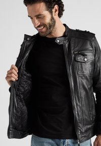 Zwarte leren jas met een gevoerde zwarte voering, ritssluiting aan de voorkant en een borstzak, met drukknoopdetails op de kraag en schouders.