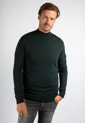 Donkergroene, aansluitende coltrui met lange mouwen. Geribbelde manchetten en zoom, gladde textuur, met een klein logo detail aan de zijkant.