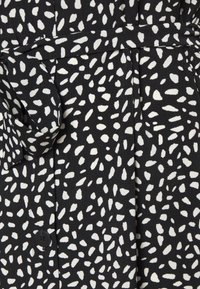 Svart tygklänning med ett vitt prickigt mönster, tygbälte och knappdetalj vid midjan, med en slät yta.