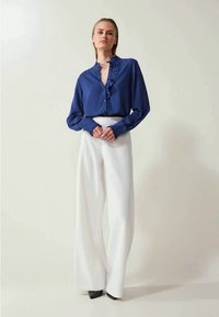 Blauwe blouse met ruches aan de sluiting, gecombineerd met hoge witte wijde broek en zwarte hakken; gladde stof en perfect passende snit.