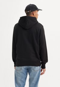Zwarte hoodie met een grote capuchon, geribbelde manchetten en zoom. Gepaard met lichtblauwe jeans, van achteren weergegeven, met een eenvoudig ontwerp.