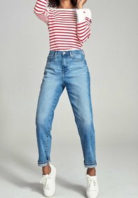 Hellblaue, hochtaillierte Jeans aus Denim mit lockerer Passform und umgeschlagenen Säumen, kombiniert mit einem rot-weiß gestreiften Langarmshirt und weißen Sneakers.