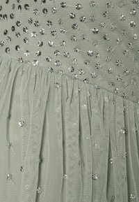 Vestido verde claro com um corpete texturizado adornado com lantejoulas prateadas e uma saia de tule com pregas para adicionar volume e movimento.