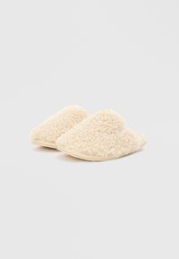 Cremefarvede hjemmesko med en tekstureret, fluffy overdel og solid beige sål, der har åben bagside for nem påtagning.