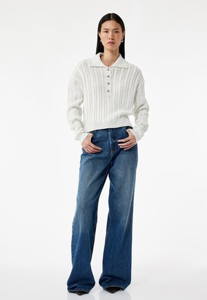 Witte gebreide pullover met een kraaghalslijn, knoopsluiting en ribbeltextuur. Gecombineerd met hooggesneden blauwe flared jeans.