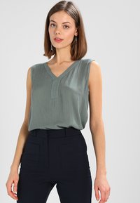 Haut sans manches en V, fabriqué en tissu mauve léger et texturé, avec un éclat subtil. Assorti à un pantalon sombre taille haute.