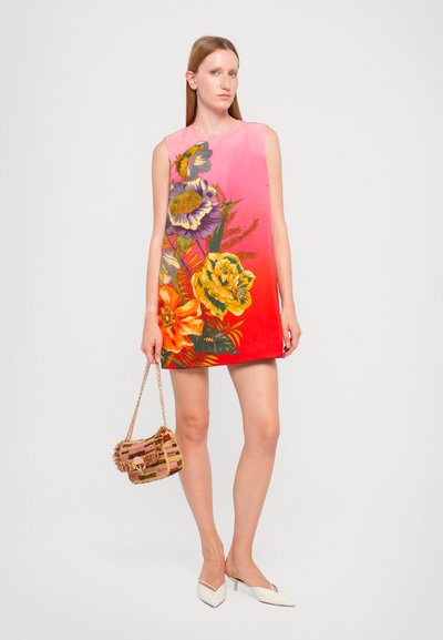 Sleeveless dress features a gradient from pink to red, adorned with colorful floral prints. Paired with a small woven handbag and white heels.