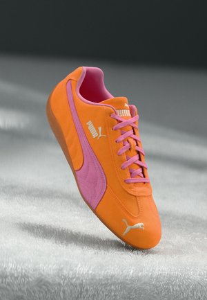 Puma-Sneaker aus leuchtend orangefarbenem Wildleder mit pinken Akzenten, ausgestattet mit flachen pinken Schnürsenkeln und einer strukturierten Oberfläche, Logo in Weiß an der Seite.