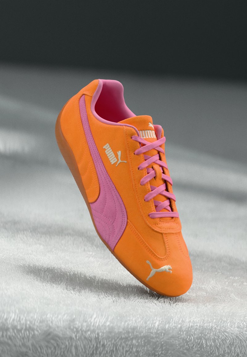 Puma sneakers in bright orange suede with pink accents, featuring flat pink laces and a textured surface, logo in white on the side.