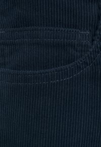 Mörk marinblå kordflorsväv med vertikal ribbning, som har en sydd fickkontur och subtil textur.