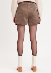 Shorts en velours côtelé marron avec une coupe ajustée et des détails cousus, associés à des bottines blanches avec un talon bloc et une fermeture à glissière.