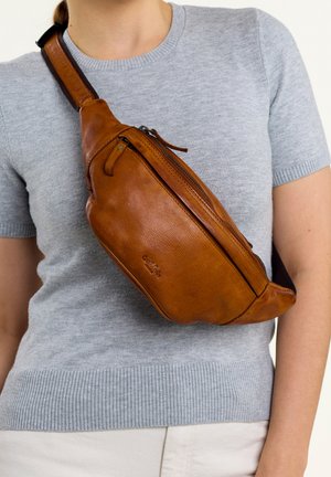 Bolso de cuero marrón tipo bandolera con un bolsillo con cremallera, forma curva y correa ajustable, llevado sobre un suéter gris.