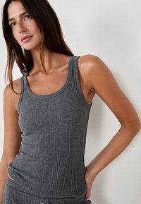 Top de tirantes gris acanalado con tirantes anchos y un diseño ajustado. La tela tiene una textura suave con una sutil elasticidad.