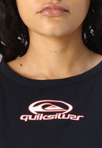 Must have musta musta T-särk musta värvi, millel on rinnal punase Quiksilveri logo. Kangas näeb välja pehme, ümarat kaelust ja lühikesed varrukad.