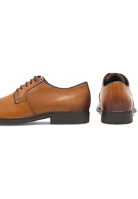 Skórzane buty eleganckie w odcieniu tan z gładką powierzchnią, okrągłym noskiem, kontrastującą ciemną podeszwą oraz sznurowadłami. Posiadają przeszyty brzeg i błyszczące wykończenie.