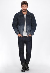 Sötét indigó színű átmenetet mutató farmerdzseki, két elülső zsebbel és klasszikus gallérral, sötét farmernadrággal és fekete csizmával párosítva.