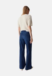 Maglione a maglia pelosa di colore chiaro con maniche corte, abbinato a jeans in denim a gamba larga di colore blu scuro, dotati di tasche posteriori e vita alta.