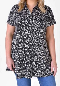 Short-sleeve black shirt featuring a white floral pattern, button front, and curved hem. Soft fabric with a relaxed fit.