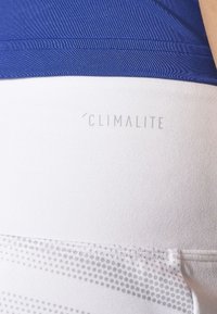 Tejido atlético blanco con una textura suave, que presenta una sección superior de color azul oscuro. La palabra "CLIMALITE" está impresa en gris.