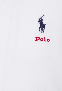 Vit bomullspolo med en marinblå broderad häst- och ryttarelogotyp med röd "Polo"-text under.