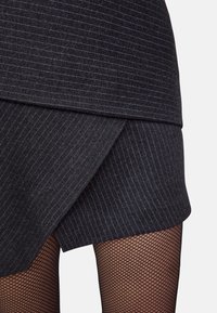Jupe à rayures gris foncé avec un design superposé et un ourlet asymétrique, associée à des collants en résille noirs.
