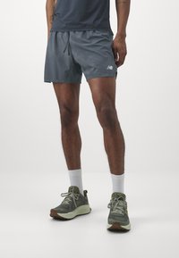 Shorts de sport gris avec une taille élastique et un cordon de serrage, associés à des chaussures de course vertes et des chaussettes blanches, sur un fond neutre.