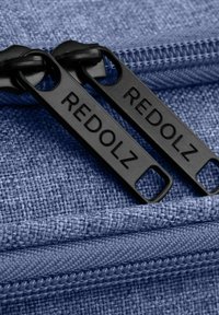 Tessuto blu testurizzato con un motivo intrecciato, caratterizzato da zip nere etichettate "REDOLZ" e una traccia di zip visibile.