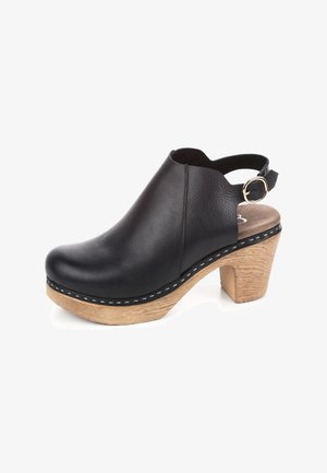 Black leather clog with an open back, wooden block heel, and white stitching along the outsole. Adjustable strap with a gold-tone buckle.