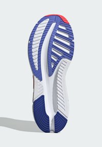 Schuhsohle mit weißem Grund und blauen sowie roten Akzenten. Verfügt über strukturierte Laufflächen, Rillen für besseren Halt und ein gebogenes Design für Flexibilität.