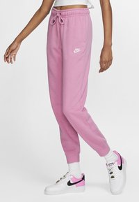 Rosa sweatpants med elastisk midjeband och dragsko, med en vit Nike-logotyp. Tillsammans med vita sneakers med rosa och svarta detaljer.