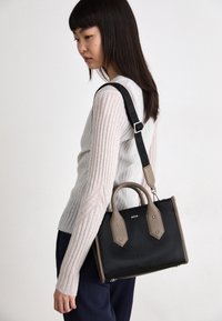 Czarna skórzana torebka z beżowymi akcentami i górnymi uchwytami, wyposażona w odpinany czarny pasek oraz logo na przedniej stronie.