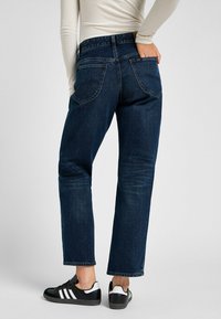 Tummansiniset farkut suoralla lahkeella, joissa on takataskut ja keskikorkea vyötärö. Yhdistetty mustiin tennareihin.