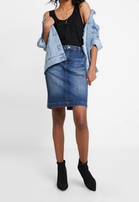 Jeanskjol i mörkblått, figurnära design, knälång. Matchad med en svart topp och en ljusblå jeansjacka. Svarta ankelskor ingår.