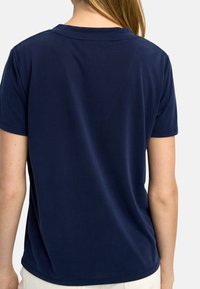 Granatowa koszula z krótkim rękawem, wykonana z gładkiego, elastycznego materiału. Posiada klasyczny okrągły dekolt oraz luźny krój z tyłu.
