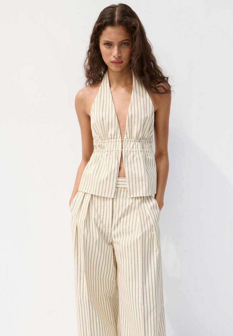 Femme portant un haut halter beige et blanc à rayures verticales et un pantalon large taille haute assorti, debout les mains dans les poches.