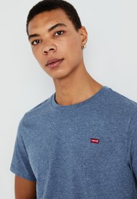 Μπλε, κοντομάνικη μπλούζα φτιαγμένη από υφασμάτινη υφή. Διαθέτει κόκκινη παρτίδα λογότυπου Levi's στην αριστερή περιοχή του στήθους. Στρογγυλή λαιμόκοψη.