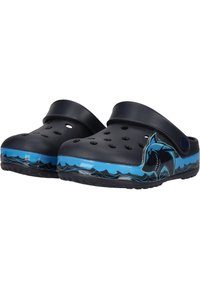 Blåa och svarta träskor av syntetiskt material med dräneringshål, design av en haj och en gummisula med vågmönster.