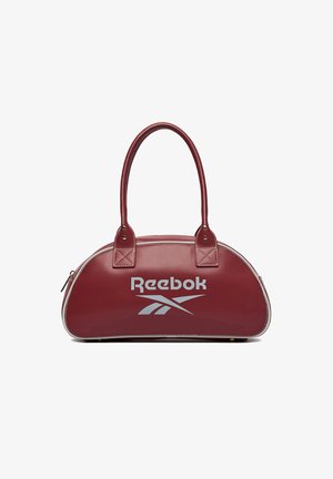 Bordowa torebka Reebok z dwoma zaokrąglonymi uchwytami, białym logo z przodu i zamkiem błyskawicznym na górze, umieszczona na białym tle.