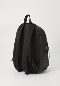 Mochila negra con respaldo acolchado y texturizado y correas ajustables. Presenta un cierre suave y un diseño de logotipo en relieve en el lateral.