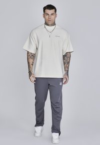 Krémové oversized tričko s krátkymi rukávmi a logom, skombinované s tmavosivými užšími nohavicami s jemným logom, doplnené bielymi teniskami.