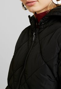 Black puffer jacket with a quilted design, featuring a high collar and zipper closure. Textured material and subtle stitched accents.
