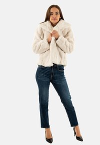 Witte nepbont jas met een brede kraag, gemêleerd oppervlak en cropped ontwerp. Draagt het met donkerblauwe jeans en zwarte hakken.