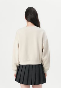 Beige avkortet genser med lange ermer, ribbestrikket hals og en teksturert overflate, kombinert med en mørk, plisserad miniskjørt.