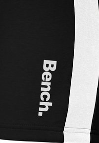 Svarta träningsshorts med vita sidpaneler som har en framträdande vit "Bench."-logotyp tryckt vertikalt på det nedre vänstra benet.
