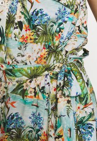 Blommig klänning med ljusgrön bakgrund, med livfulla tropiska mönster, knytmidja, ficka och texturerad tyg.